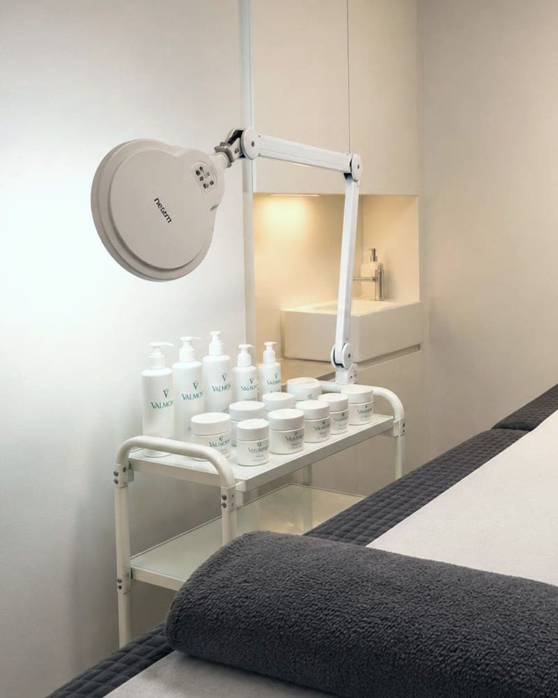 A treatment room at Pure Essentials London with a product trolley and a magnifier lamp